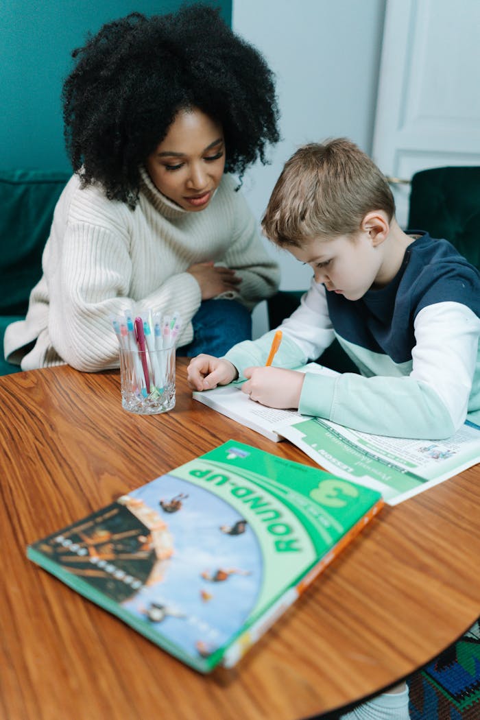 A woman helps her son with his homework at a table, fostering learning and understanding.